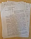 A yellowed typewritten document with handwritten notes lies on top of several sheets of paper on a light-coloured surface.
