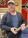 Steinar Grønnås stands indoors holding a rusty piece of metal from Tirpitz.