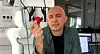 A man holds a small red object beside a white robotic arm in a laboratory.