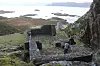 Stone ruins of St. Sunniva Church on a hillside above the coast, with a person examining the foundation.