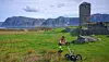 Person operating ground-penetrating radar in a grassy field near a stone tower on Selja.