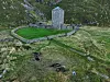 A stone tower with a blue roof sits inside a low stone wall on a grassy hillside.