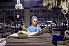 Worker in blue uniform standing behind stacked fabric rolls inside a textile factory.