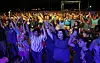 Large crowd at an outdoor Christian gathering, raising their hands in prayer in the evening.