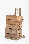 Stacked wooden crates in a worn wooden carrier with rope and a metal frame stand against a white background.
