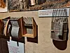 Old agricultural tools hang on a wall with informational signs beneath them.