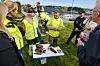 People in hi-vis jackets stand around a table with debris during an outdoor briefing.