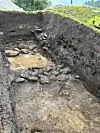 A deep excavation trench showing exposed stones and earth at an outdoor dig site.