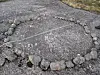 An irregular stone outline on cracked asphalt near grass.