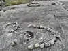 Small stones arranged in a spiral on a large weathered rock outdoors.