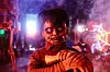Person in a horror costume with face paint and glowing neon lights in the background.