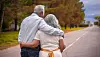Couple walking arm in arm along a tree-lined road with countryside in the distance.