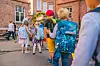Schoolchildren with colourful backpacks gather in the schoolyard by a red brick building.