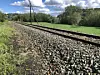 Railway tracks extend through a green countryside landscape beneath a partly cloudy sky.