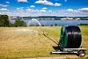 An irrigation reel sprays a dry grain field beside a lake in Eastern Norway.