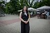 Yuliia Palaniuk stands in a paved café courtyard with outdoor seating and trees behind her.