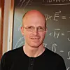Portrait photo of Johannes Skaar in front of a blackboard covered with equations.