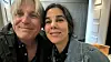 Two smiling adults take a selfie indoors against a modern interior backdrop.