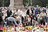 Crowd gathers behind a colourful tribute of flowers, candles and Norwegian flags in Oslo.