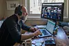 Man wearing headphones works on laptops at a home-office desk in Oslo.