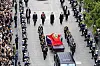 A red-draped coffin travels through Oslo in a ceremonial procession surrounded by guards, officials and crowds.