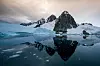 Snow-covered mountain and its reflection in a calm, ice-dotted glacial lake.