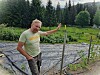 Farmer Erik Røed gestures beside vegetable beds in a forested rural garden.