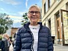 Toril Moe, 75, wearing glasses and a navy puffer jacket outdoors beside a modern building.