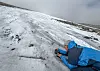 An archaeologist lies on her stomach on the ice to photograph an arrow shaft lying in the ice.
