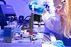 Gloved scientist operating precision laboratory equipment under blue lighting.
