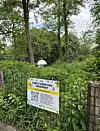 Insect sampling sign fixed to a fence beside dense greenery and woodland.