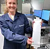 Smiling SINTEF researcher holding a pouch battery cell beside laboratory equipment and computer screens.