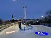 Blue and red illuminated symbols mark a bridge walkway beside railings at dusk.