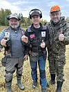Photo of two metal detectorists and the owner of the field they are standing in. One of them is holding a coin in his hand.