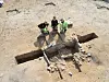 Three archaeologists in high-vis clothing at an excavation with stones and a narrow trench.