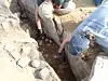 Two archaeologists examine a narrow stone cist during an archaeological excavation.