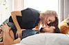 Young couple kissing in bed. They are wearing clothes, and she is lying on top of him.