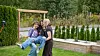 Three people pose beside a trellis in a landscaped garden with raised flower beds.