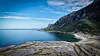 Sheltered blue bay beneath a forested mountain, with a sandy beach and rocky foreground.