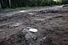 White survey marker with a red stake on muddy cleared ground near trees