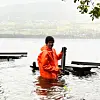 Researcher in an orange jacket stands in Lake Vangsvatnet beside floating equipment.