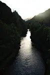 The Vosso River glistens through a dark forested valley beneath low sunlight.