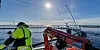A safety-clad researcher stands beside red equipment on the service vessel Torra at a marine fish-farming site.