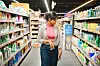 Woman examining cleaning products in a grocery store, with shelves on both sides.