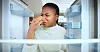 Woman covering her nose while looking into an open refrigerator.