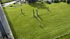 A manicured green lawn with fence posts, trees and part of a building at the left edge.