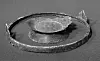 Weathered circular metal object with a raised centre on a textured surface.