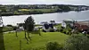 Green hillside with houses overlooking calm water and a wooded opposite shore.