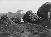 Black-and-white scene of a person among rocks, with a house and framework in the background.