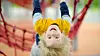 Blond child in a yellow sweater hanging upside down on an indoor climbing frame.